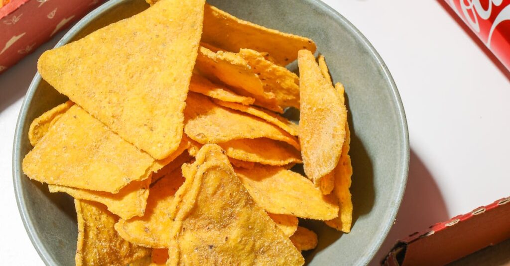 pexels-photo-4109117-4109117 A bowl of tortilla chips with pizza and cola cans, perfect for a party snack.